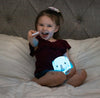 Child holding LumiElephant nightlight glowing blue while operating remote.