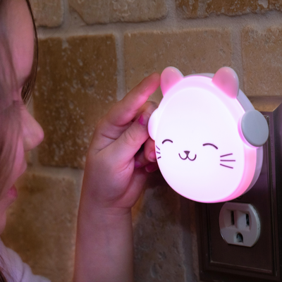 Child touching the ear of the LumiGlow cat while plugged in and glowing pink.